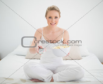 Natural smiling blonde holding remote and popcorn