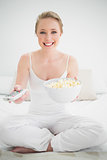 Natural cheerful blonde holding remote and popcorn