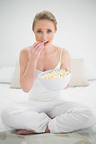 Natural cheerful blonde eating popcorn on bed