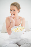 Natural happy blonde eating popcorn on bed