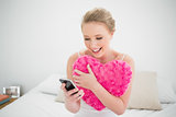 Natural smiling blonde holding heart pillow and smartphone