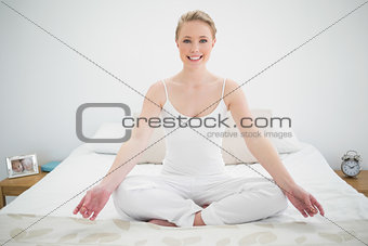 Natural smiling blonde meditating on bed