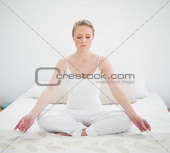 Natural peaceful blonde meditating on bed