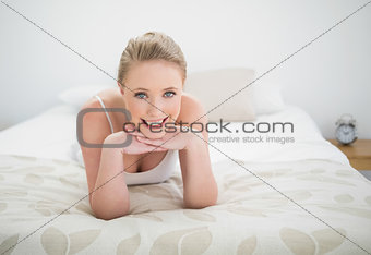 Natural smiling blonde lying on bed touching her chin