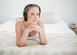 Natural smiling blonde lying on bed and listening to music
