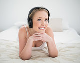 Natural cheerful blonde lying on bed and listening to music