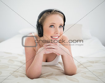 Natural cheerful blonde lying on bed and listening to music