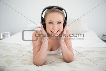 Natural happy blonde lying on bed and listening to music