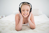 Natural happy blonde lying on bed and listening to music with closed eyes