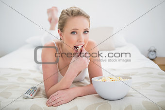Natural happy blonde lying on bed and eating popcorn