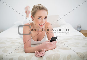 Natural cheerful blonde lying on bed and using smartphone