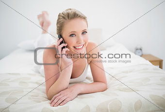 Natural cheerful blonde lying on bed and phoning
