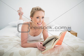Natural smiling blonde reading a book and lying on bed