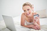 Natural smiling blonde holding credit card and looking at laptop