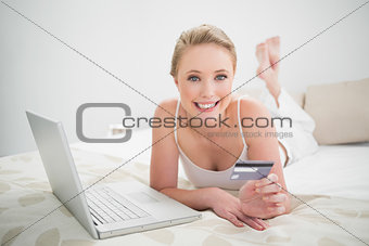 Natural cheerful blonde holding credit card and looking at camera