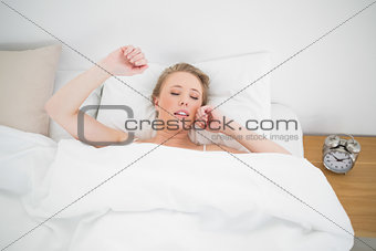 Natural yawning blonde lying in bed with closed eyes