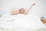 Natural yawning blonde lying in bed with closed eyes and stretched arms