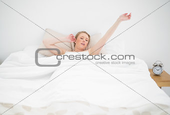 Natural yawning blonde lying in bed with closed eyes and stretched arms