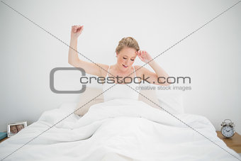 Natural yawning blonde sitting in bed with closed eyes