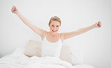 Natural smiling blonde sitting in bed and stretching her arms