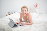 Smiling natural blonde lying on bed and using tablet