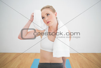 Thoughtful sporty blonde touching forehead with towel