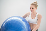 Smiling sporty blonde holding exercise ball and looking at it