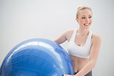 Smiling sporty blonde holding exercise ball and looking away