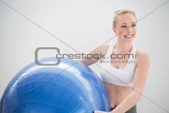 Smiling sporty blonde holding exercise ball and looking away