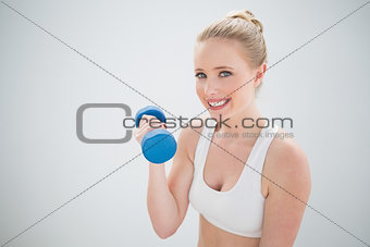 Smiling sporty blonde holding dumbbell