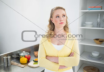Thoughtful cute blonde standing with arms crossed