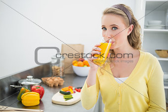 Content cute blonde drinking a glass of orange juice