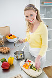 Smiling cute blonde putting vegetables in a pot