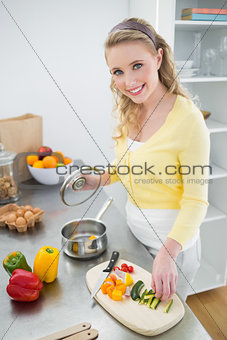 Smiling cute blonde putting vegetables in a pot
