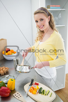 Smiling cute blonde stirring with wooden spoon