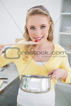 Cheerful cute blonde tasting food from wooden spoon