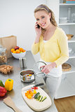 Cheerful cute blonde phoning and making dinner