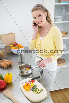 Cheerful cute blonde phoning and making dinner