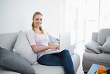 Casual smiling blonde sitting on couch using laptop