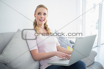 Casual pretty blonde sitting on couch using laptop