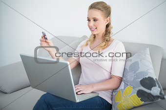 Casual smiling blonde holding laptop and credit card