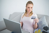 Casual content blonde holding laptop and looking at credit card