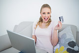Casual excited blonde holding laptop and credit card