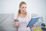 Casual thrilled blonde holding tablet and credit card