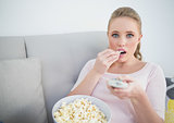 Casual astonished blonde holding remote and eating popcorn