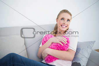 Casual day dreaming blonde holding heart pillow