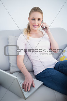 Casual cheerful blonde phoning and using laptop