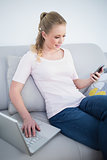 Casual smiling blonde using smartphone and laptop