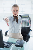 Blonde stern businesswoman showing calculator and thumb down