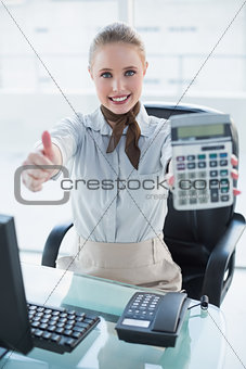 Blonde smiling businesswoman showing calculator and thumb up